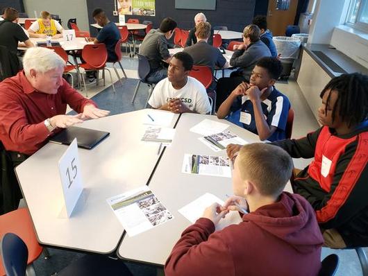 This is a photo of four male students sitting at a round table listening to their Career Coach.