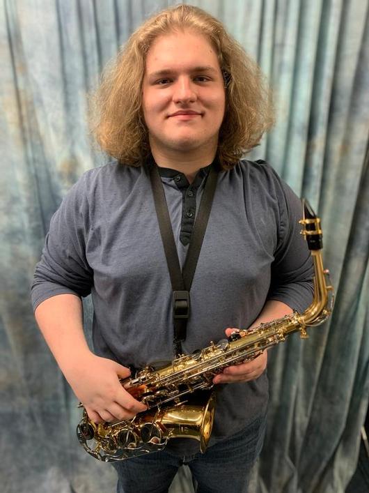 This is a photo of ITC student composer Zayde, holding his instrument and smiling at the camera.