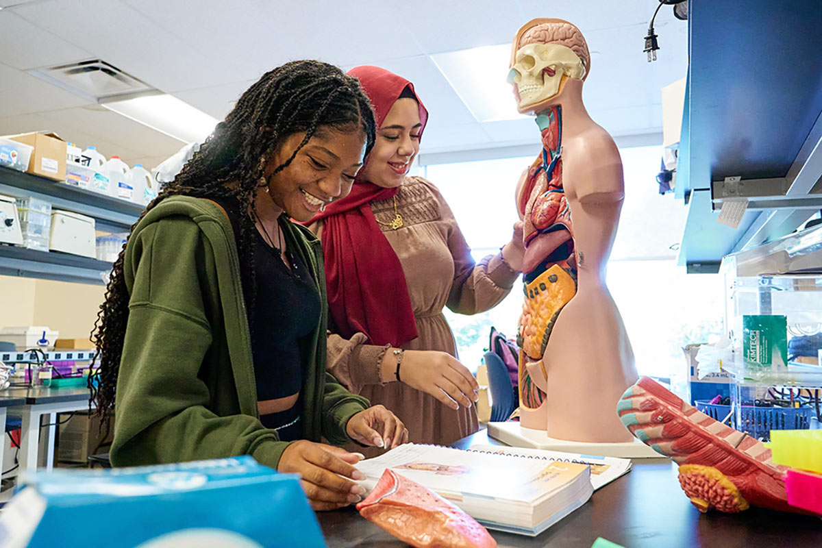 This is a photo of two female students working in a health classroom, smiling as they take notes.